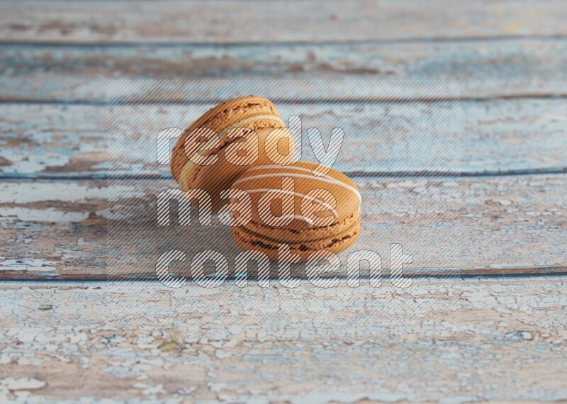 45º Shot of of two assorted Brown Irish Cream, and light brown Almond Cream macarons next to each other on light blue background