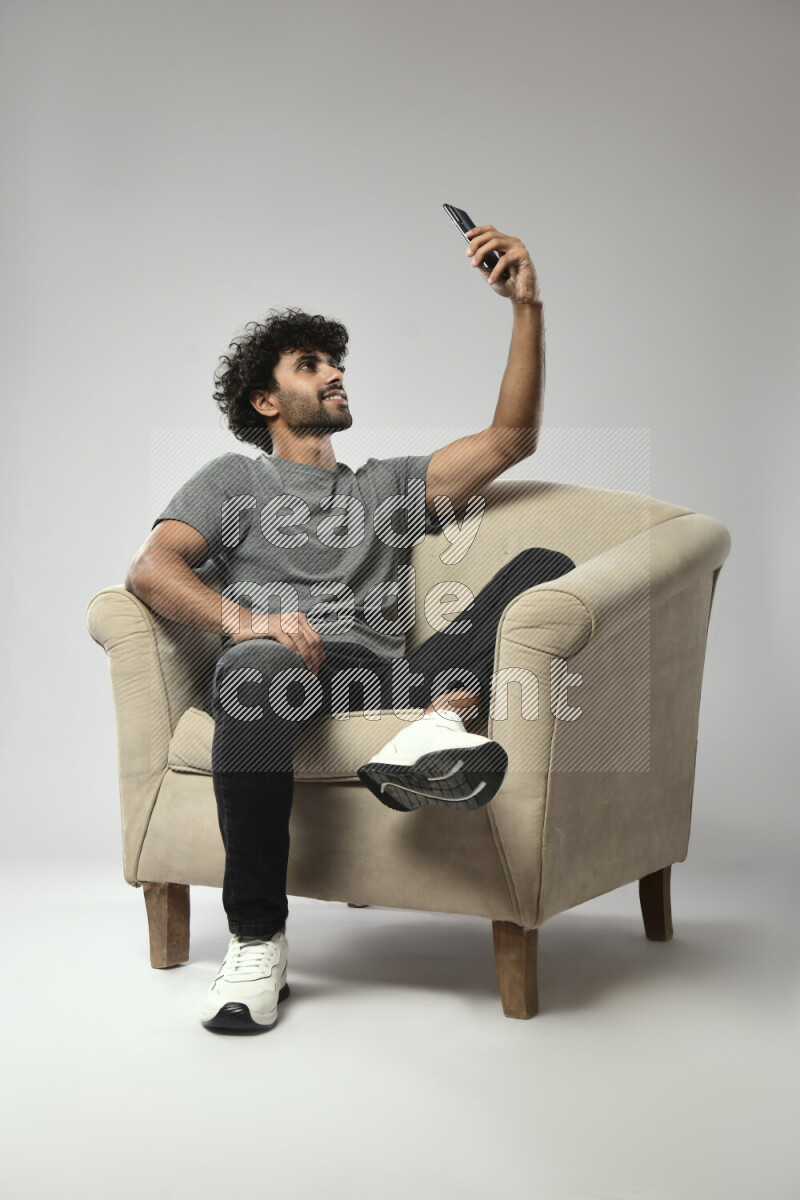 A man wearing casual sitting on a chair taking a selfie on white background