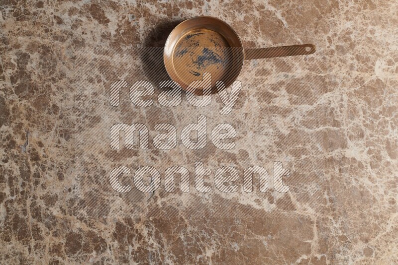 A small copper pan on beige marble background