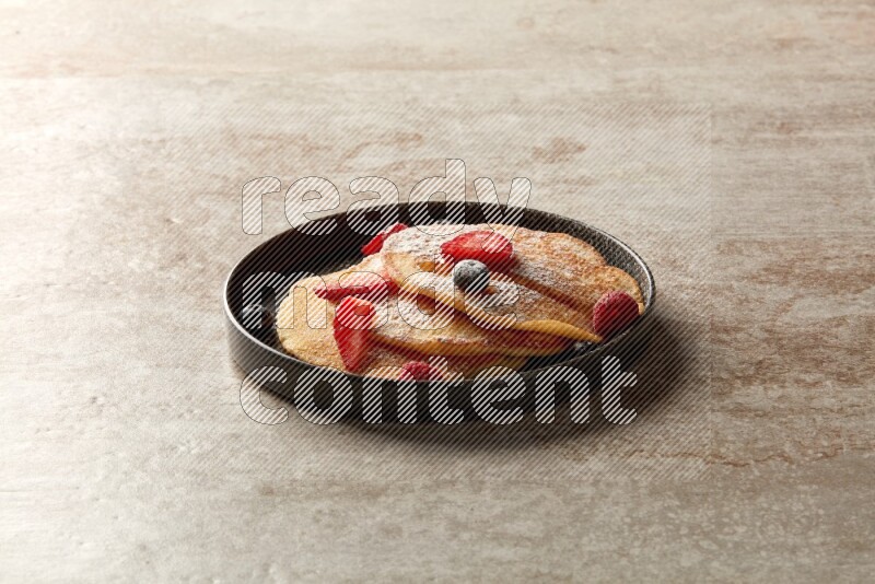 Three stacked mixed berries pancakes in a black plate on beige background