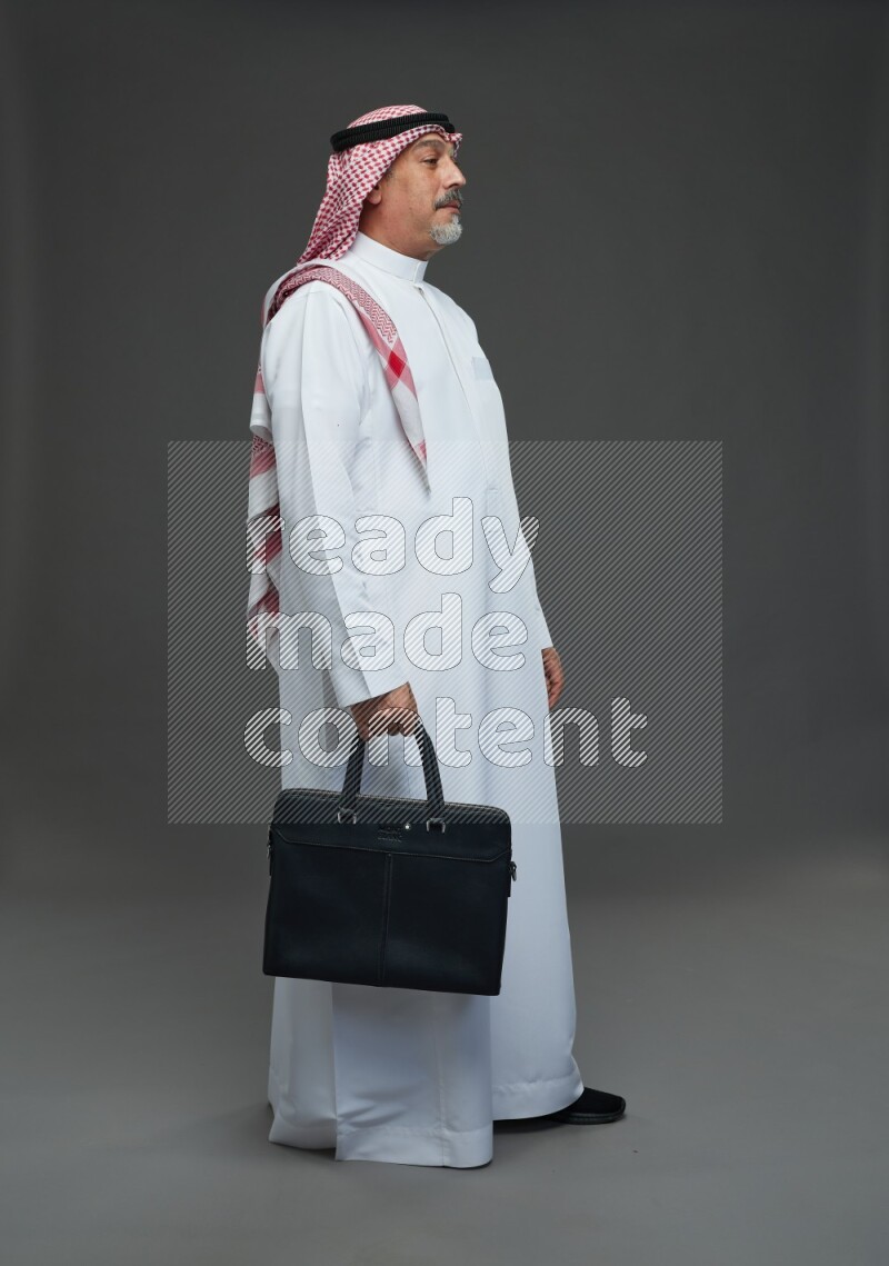 Saudi man with shomag Standing holding bag on gray background