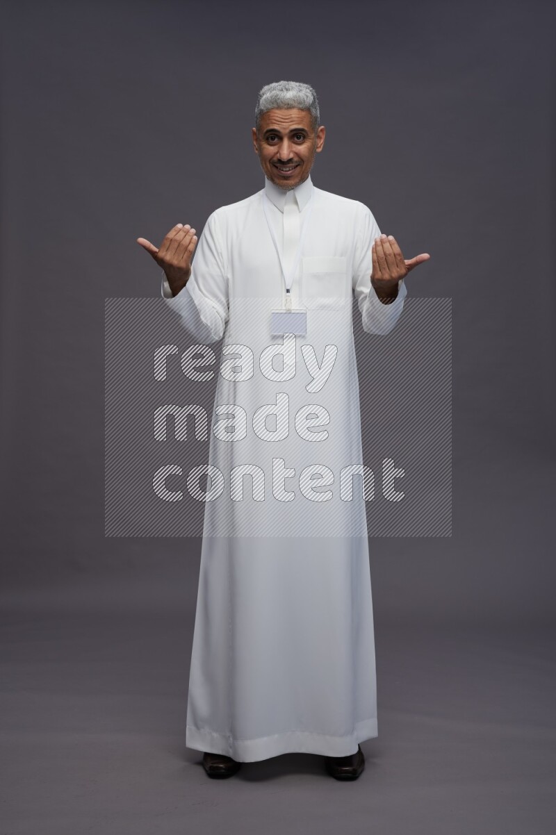 Saudi man wearing thob with neck strap employee badge standing interacting with the camera on gray background