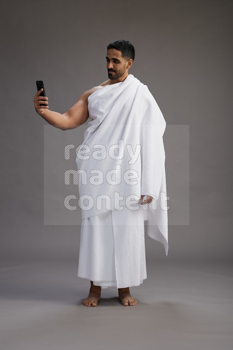 A man wearing Ehram Standing texting on phone on gray background
