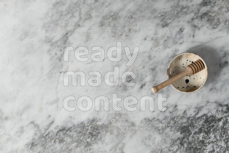 Multicolored pottery bowl with wooden honey dipper in it on grey marble background