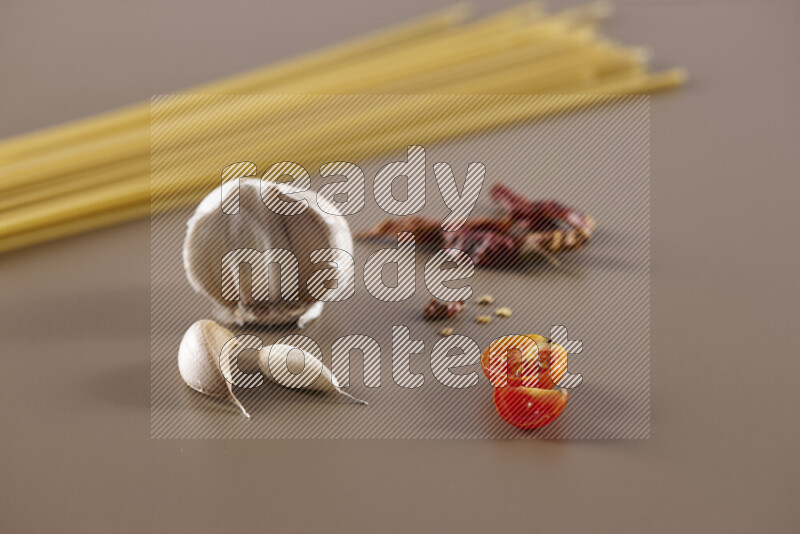 Raw pasta with different ingredients such as cherry tomatoes, garlic, onions, red chilis, black pepper, white pepper, bay laurel leaves, rosemary and cardamom on beige background