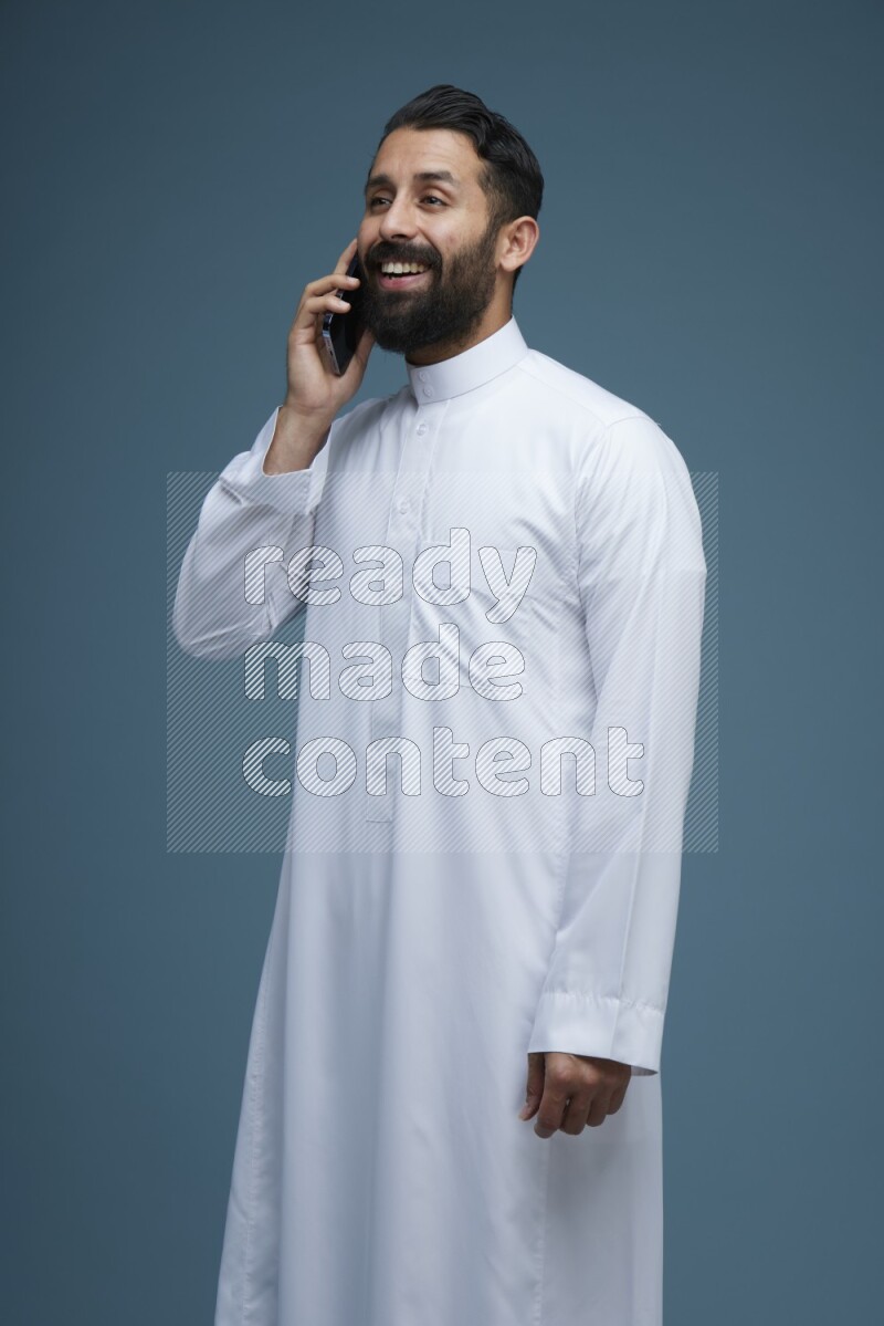 A man having a call on a blue background wearing Saudi Thob