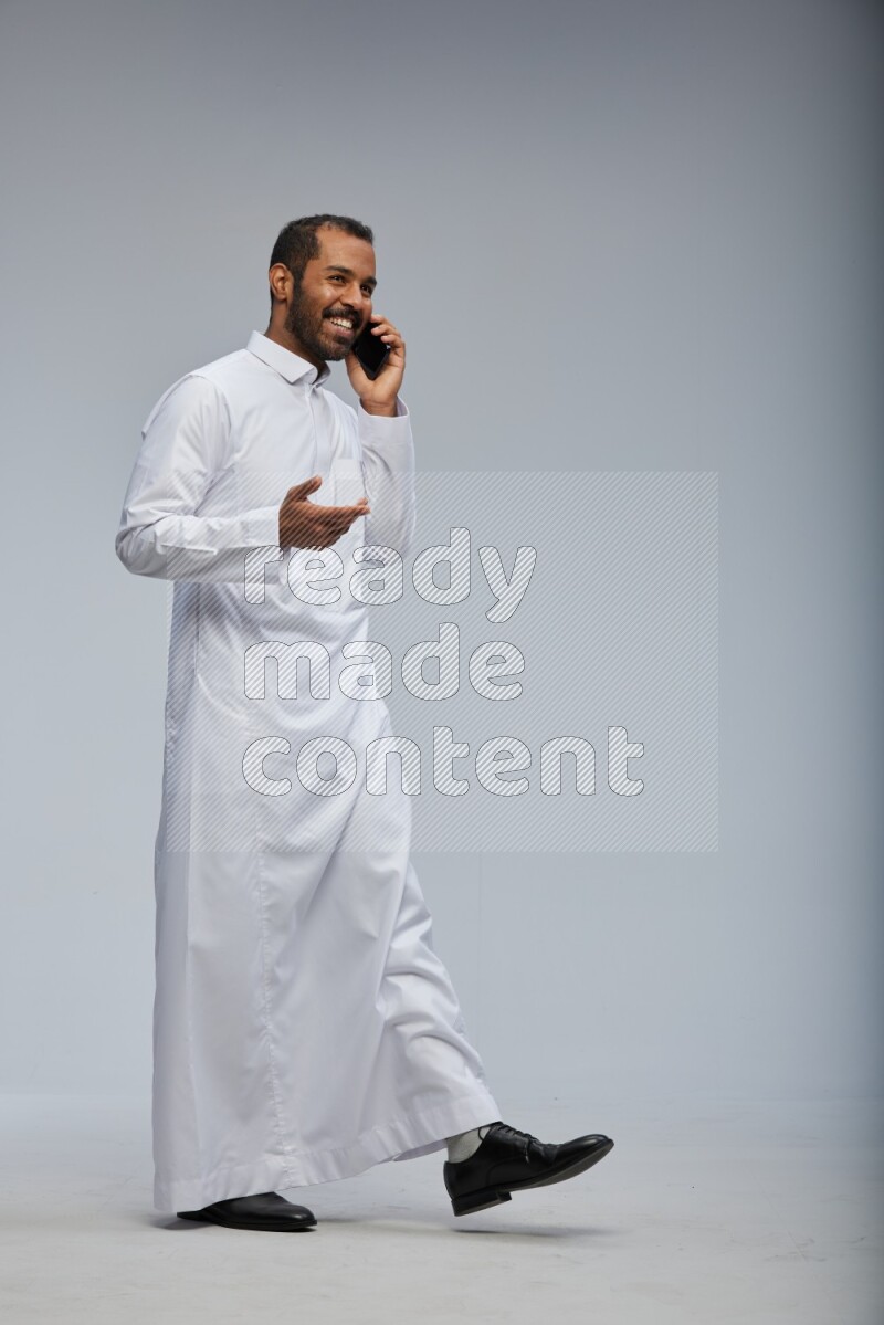 Saudi man wearing Thob standing talking on phone on Gray background