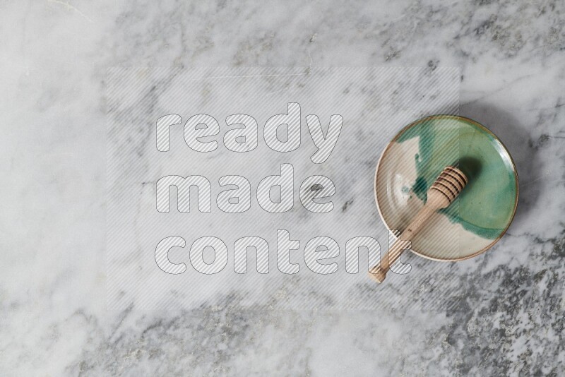 Multicolored pottery plate with wooden honey dipper in it on grey marble background