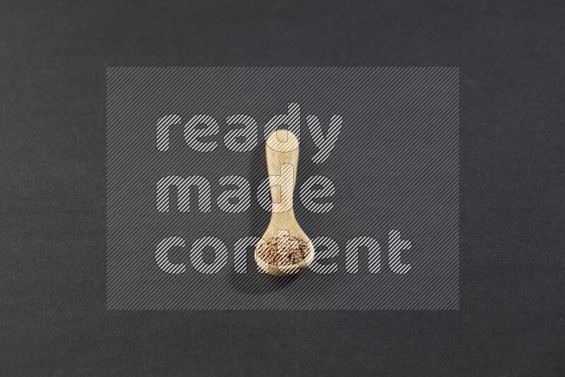 A wooden spoon full of mustard seeds on a black flooring