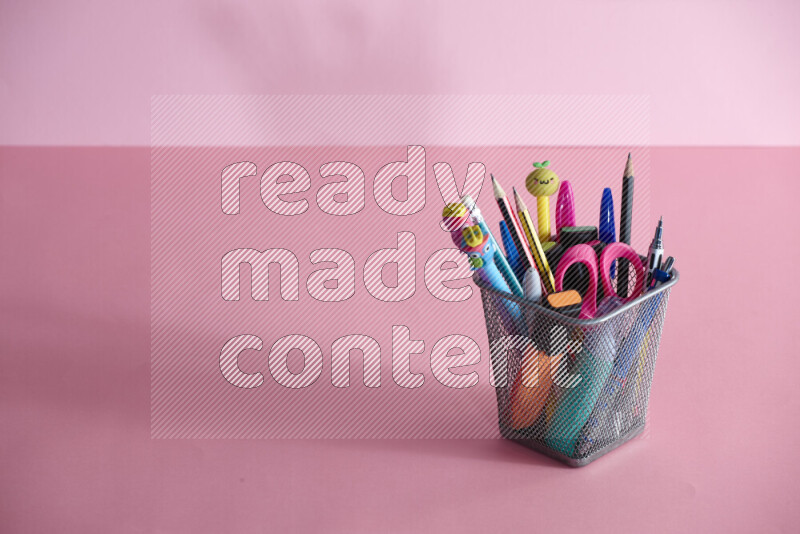 Pens, pencils and other different school supplies in a metal pen holder on rose background