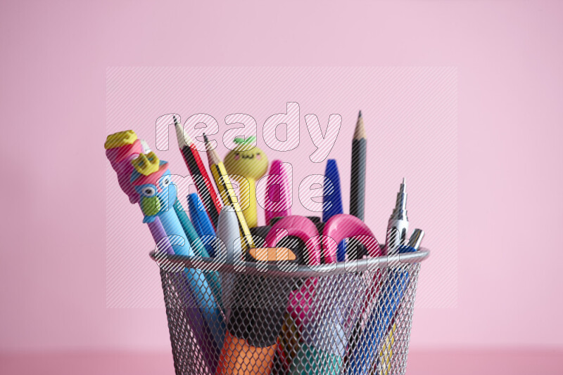 Pens, pencils and other different school supplies in a metal pen holder on rose background