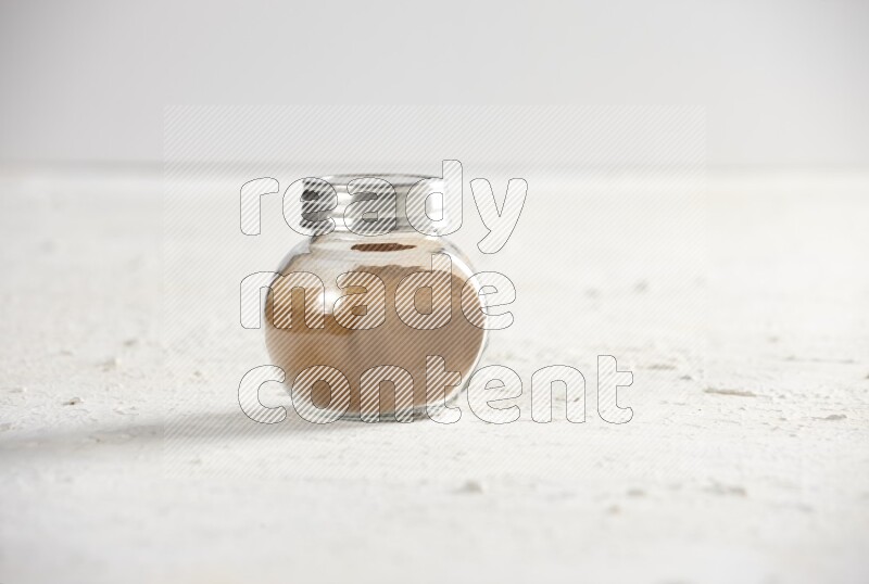 Herbs glass jar full of cinnamon powder on a textured white background