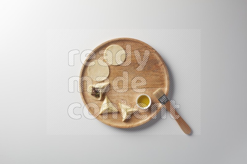 two closed sambosas and one open sambosa filled with meat while oil with oil brush aside in a wooden dish on a white background