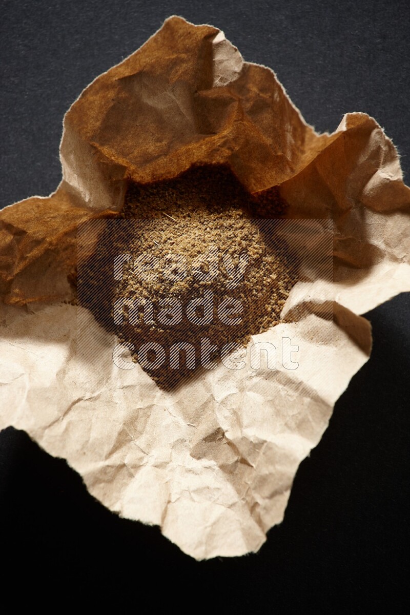 Cumin powder in a crumpled piece of paper on black flooring