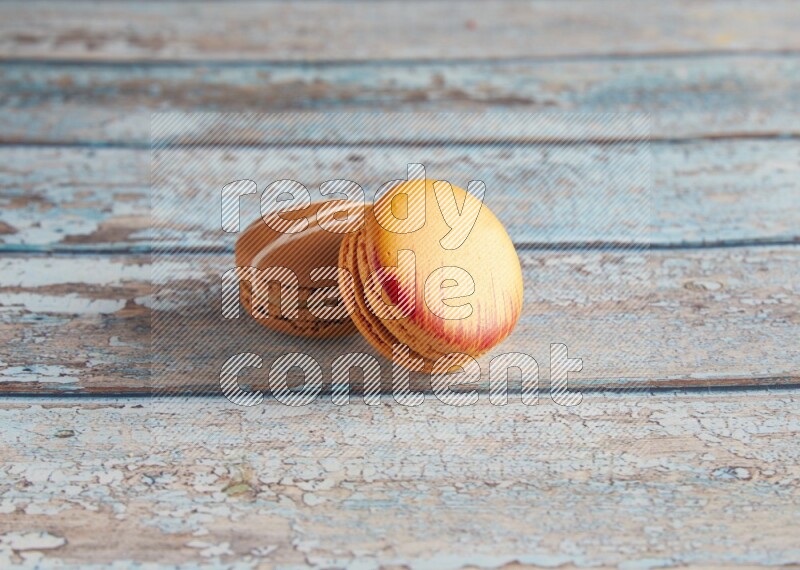 45º Shot of of two assorted Brown Irish Cream, and Orange Exotic macarons on light blue background