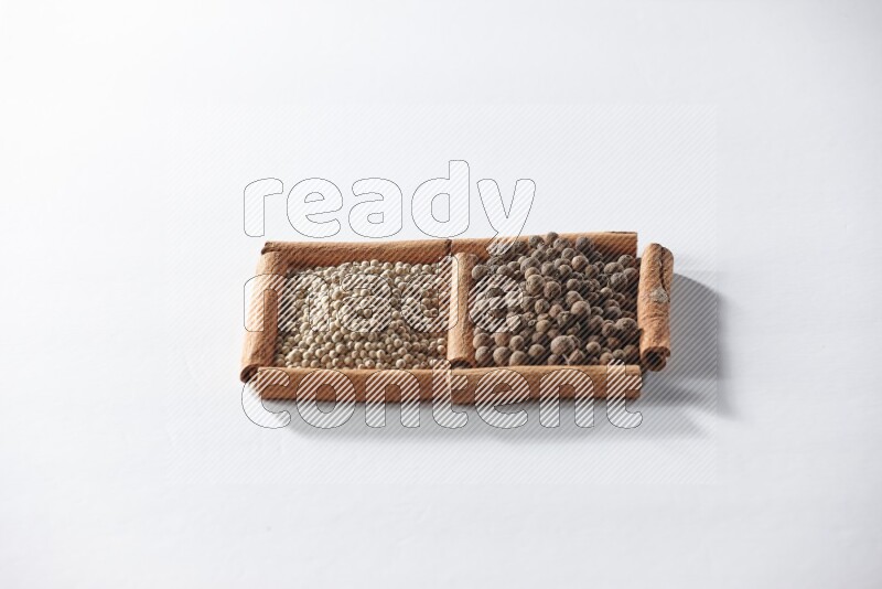 مربعان من أعواد القرفة ممتلئان بحبوب الفلفل الأبيض وحبوب الفلفل الحلو علي خلفية بيضاء