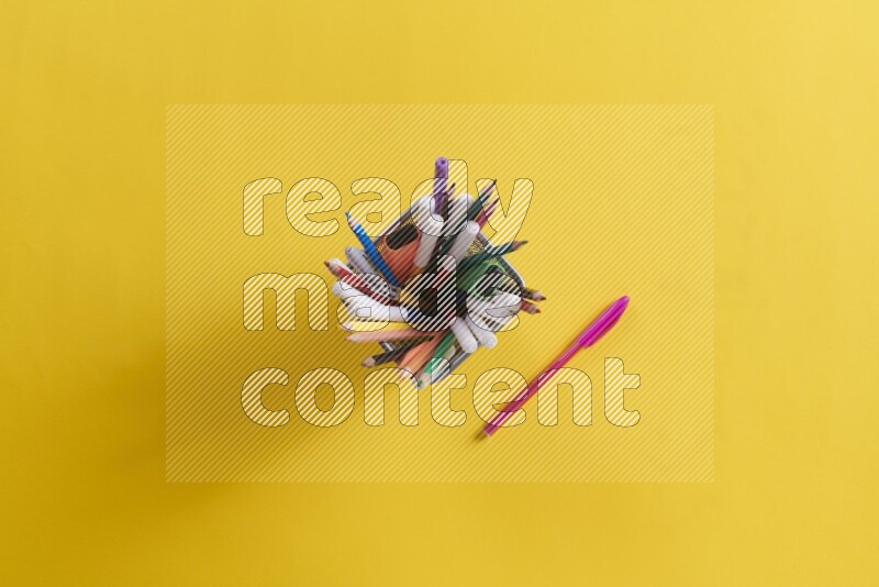 بعض الأقلام والمستلزمات المدرسية في مقلمة معدنية علي خلفية صفراء