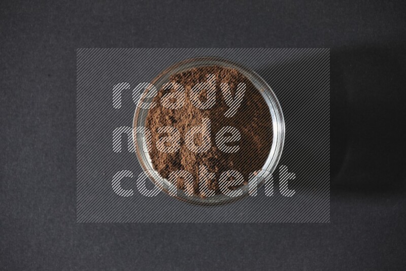A glass bowl full of cloves powder on black flooring