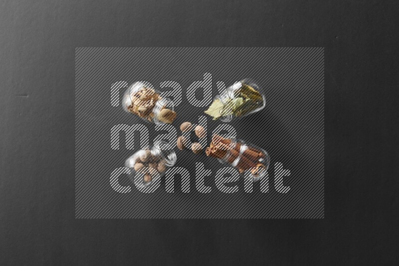 4 glass spice jars full of laurel bay leaves, ginger, cinnamon and nutmeg on black flooring