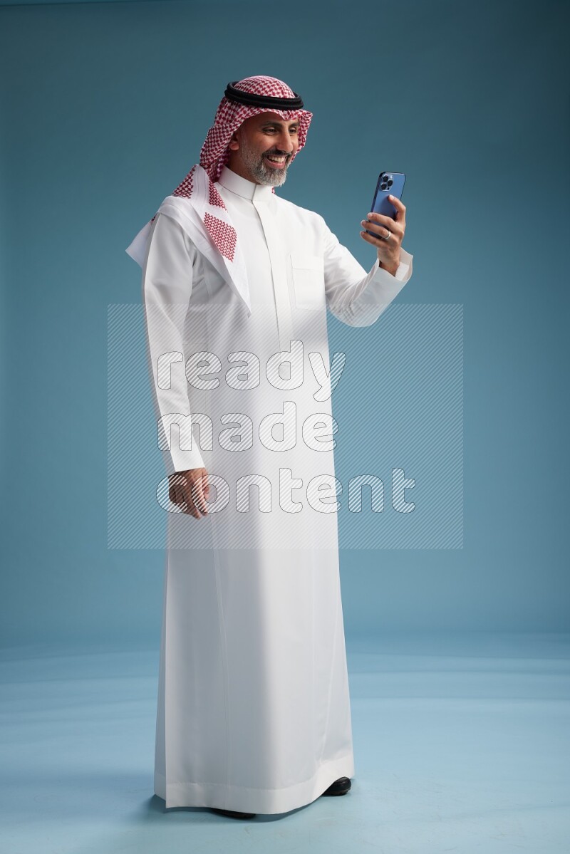 Saudi man wearing thob and shomagh texting on blue background