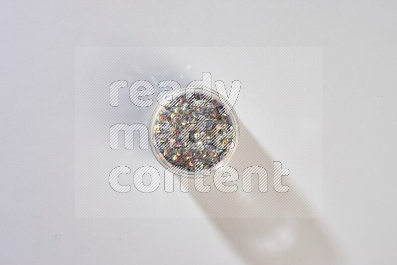Colored flat sequins in a glass jar on grey background
