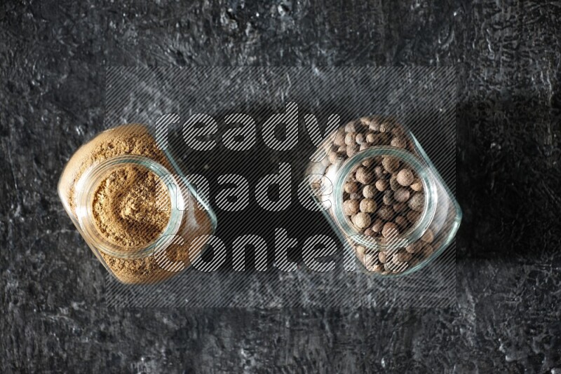 وعاءان زجاجيان للتوابل ممتلئان ببودرة بهار الفلفل الحلو وحبوبه على خلفية سوداء