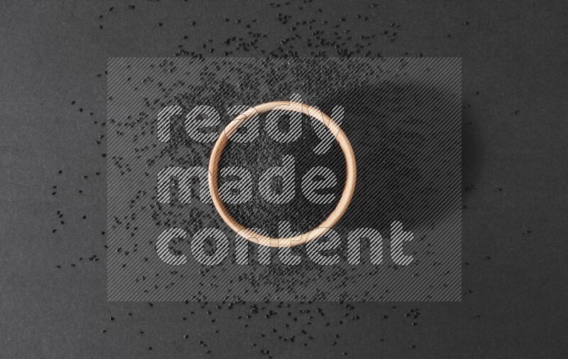 وعاء خشبي ممتلئ ببذور حبة البركة محاط ببعض البذور علي خلفية سوداء