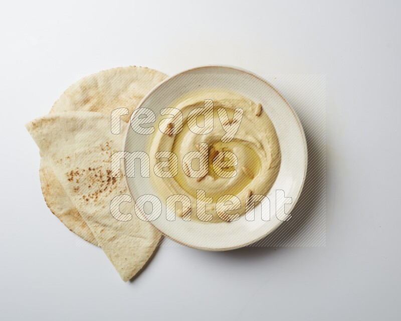 Hummus in a pottry plate garnished with pine nuts on a white background