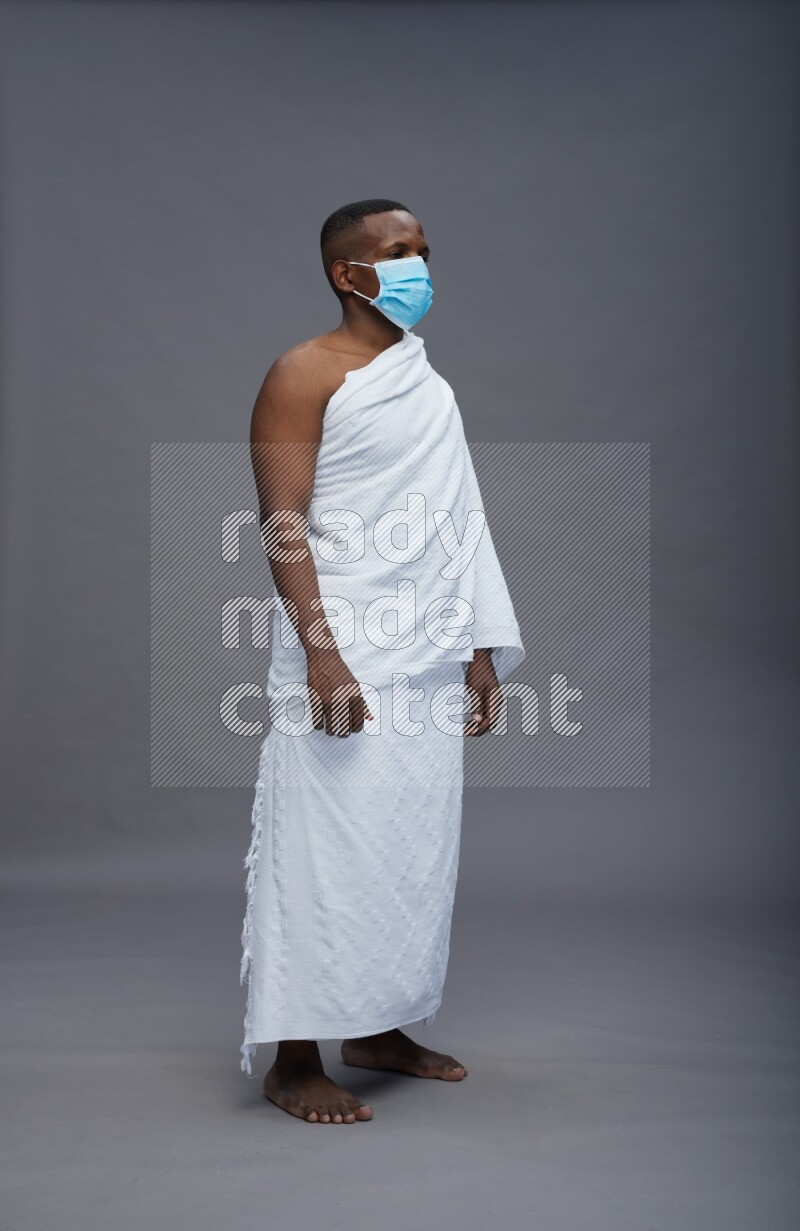A man wearing Ehram with face mask Standing Interacting with the camera on gray background