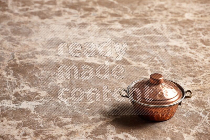 A small copper pot on beige marble background