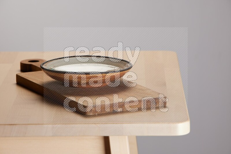 multi-colored pottery Plate placed on a  wooden rectangular cutting board on the edge of wooden table
