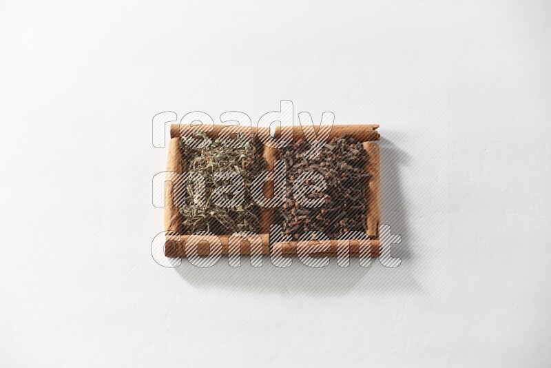 2 squares of cinnamon sticks full of cloves and dried basil on white flooring