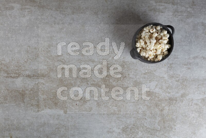 popcorn in a black handheld ceramic bowl on a grey textured countertop