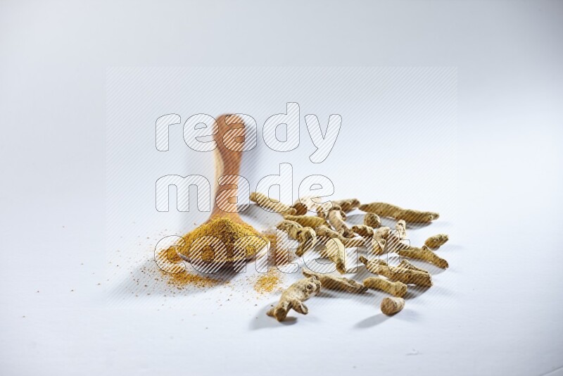 A wooden ladle full of turmeric powder and dried turmeric fingers beside it on white flooring