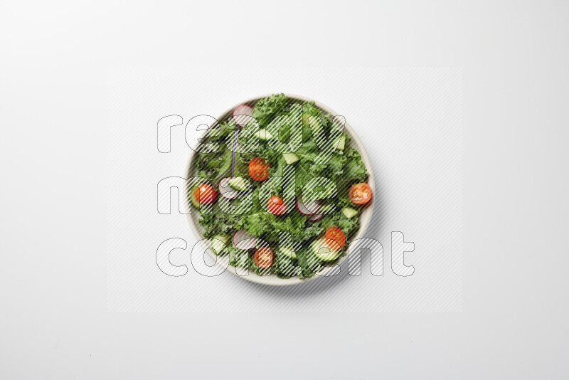 A bowl of fresh vegetables salad with kale leaves, cherry tomatoes, sliced radishes and sliced cucumber on a white background