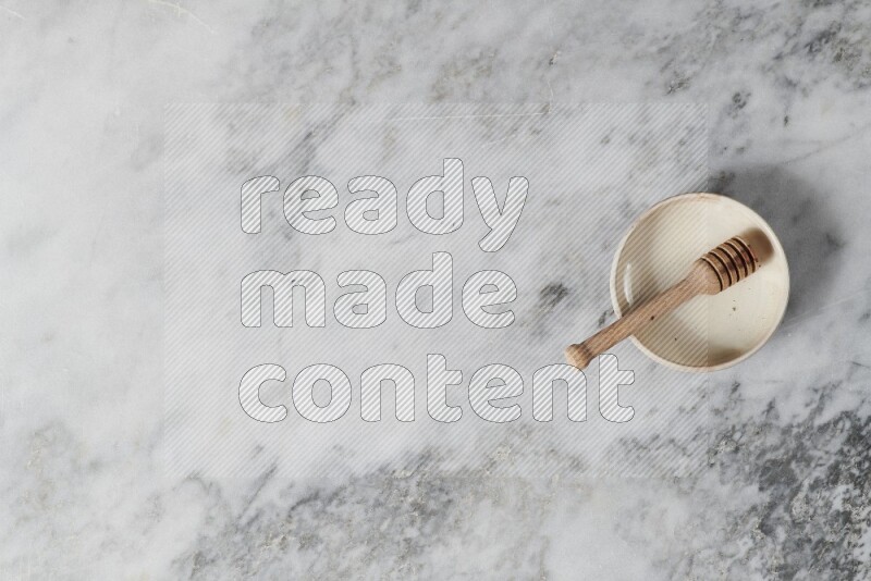 Beige pottery bowl with wooden honey dipper in it on grey marble background