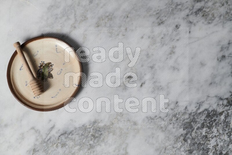 Decorative pottery plate with wooden honey dipper in it on grey marble background