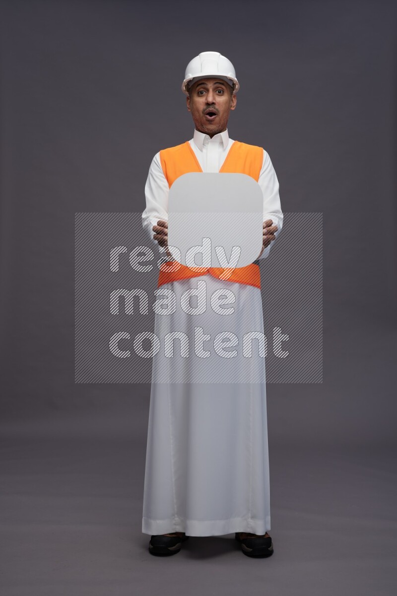Saudi man wearing thob with engineer vest standing holding social media sign on gray background