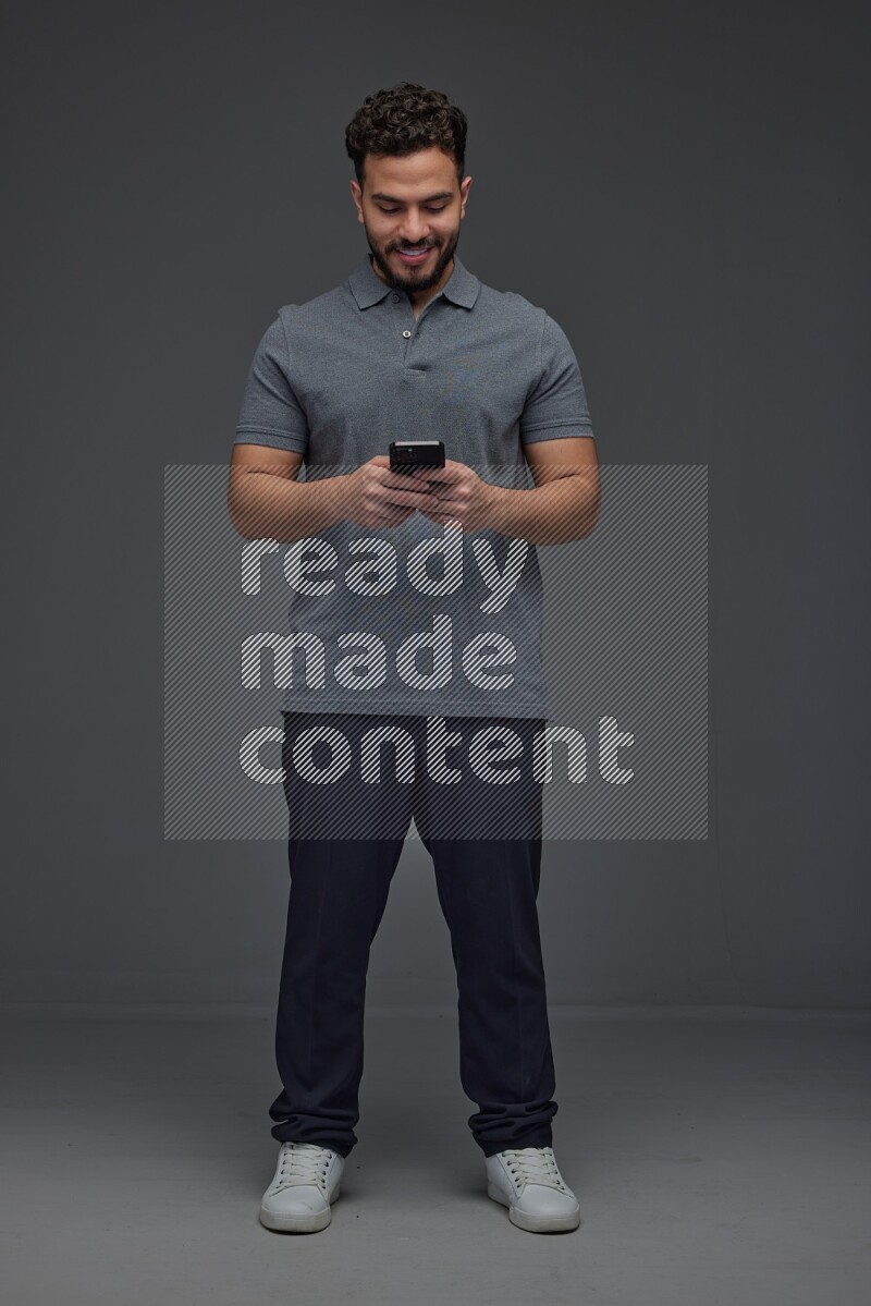 A man wearing casual standing and using his phone eye level on a gray background