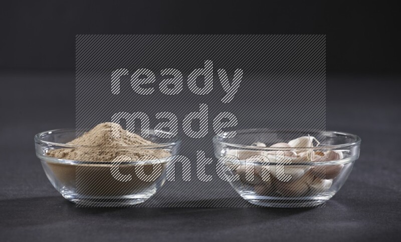 2 glass bowls, one full of garlic powder and the other full of garlic cloves on a black flooring