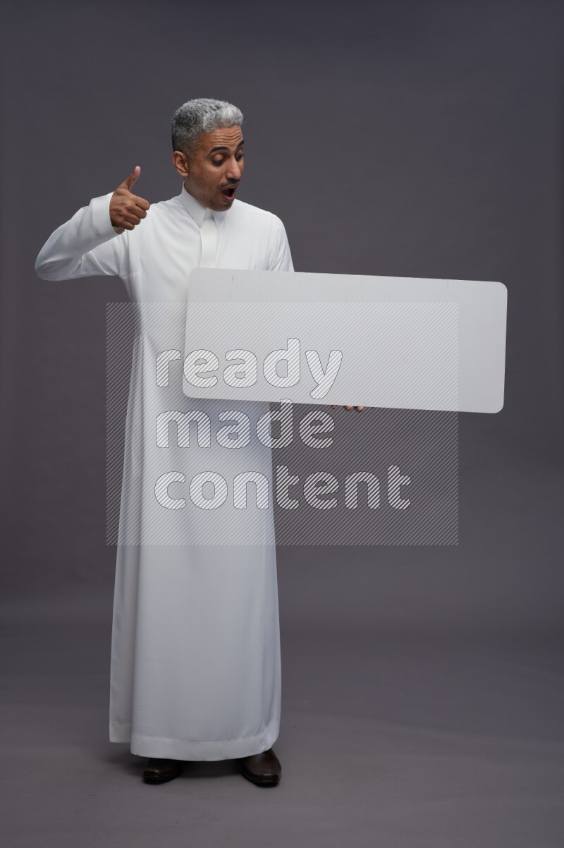 Saudi man wearing thob standing holding board on gray background