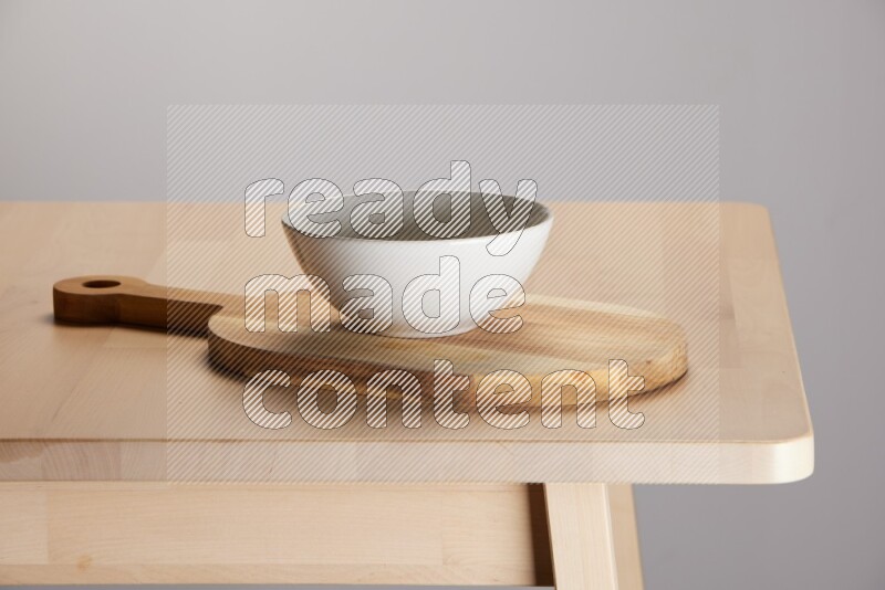 off white bowl placed on a  wooden oval cutting board on the edge of wooden table