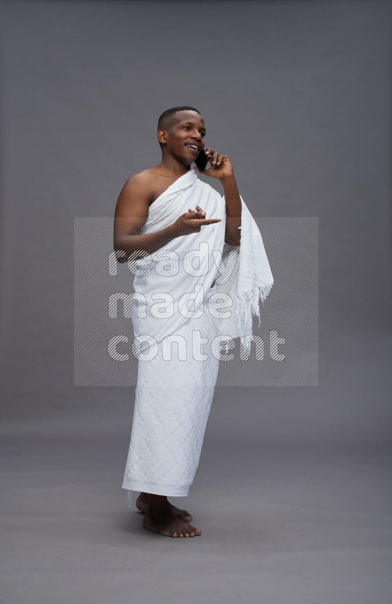 A man wearing Ehram Standing talking on phone on gray background