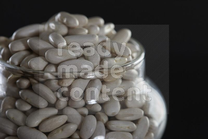 White beans in a glass jar on black background