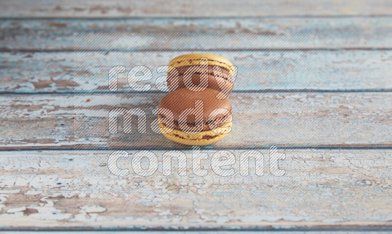 45º Shot of two Yellow and Brown Chai Latte macarons on light blue wooden background