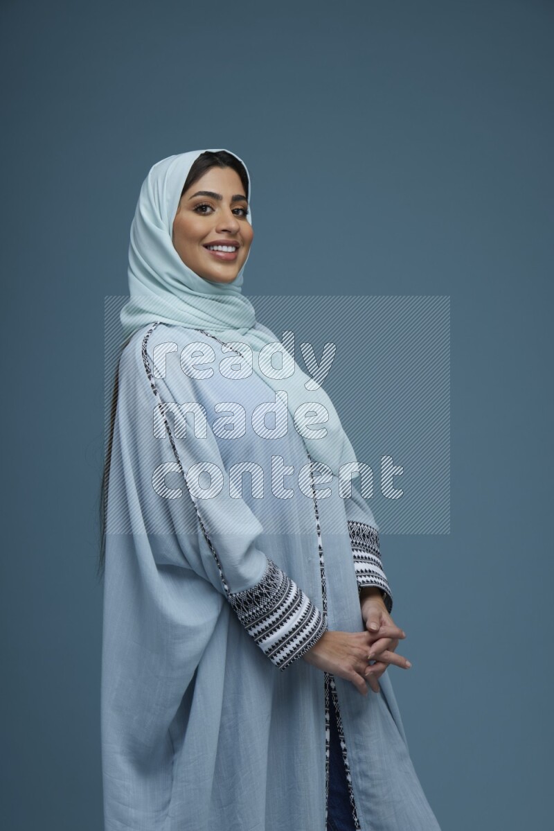 A woman posing in a blue background wearing a blue Abaya with hijab