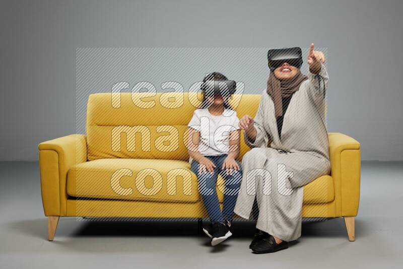 A girl and her mother sitting playing with VR on gray background