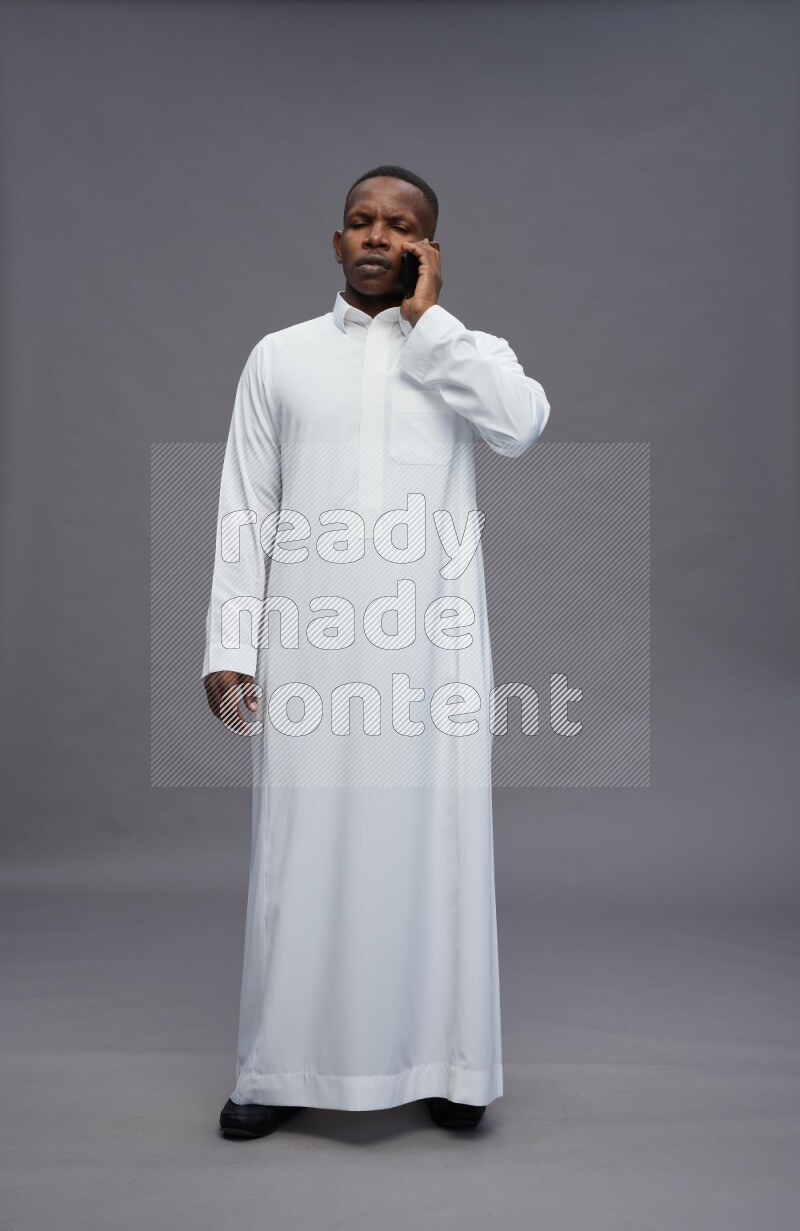 Saudi man wearing thob standing talking on phone on gray background