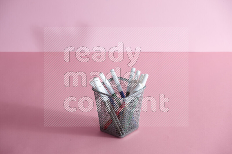 Pens, pencils and other different school supplies in a metal pen holder on rose background