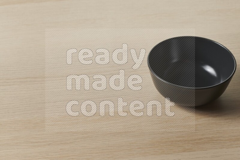A black ceramic bowl on light wooden background